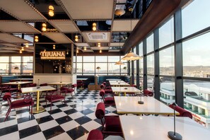 A spacious restaurant with checkered flooring, multiple seating areas, and large windows offering a view of the cityscape. - Hotel Indigo Tijuana Downtown by IHG (Tijuana)
