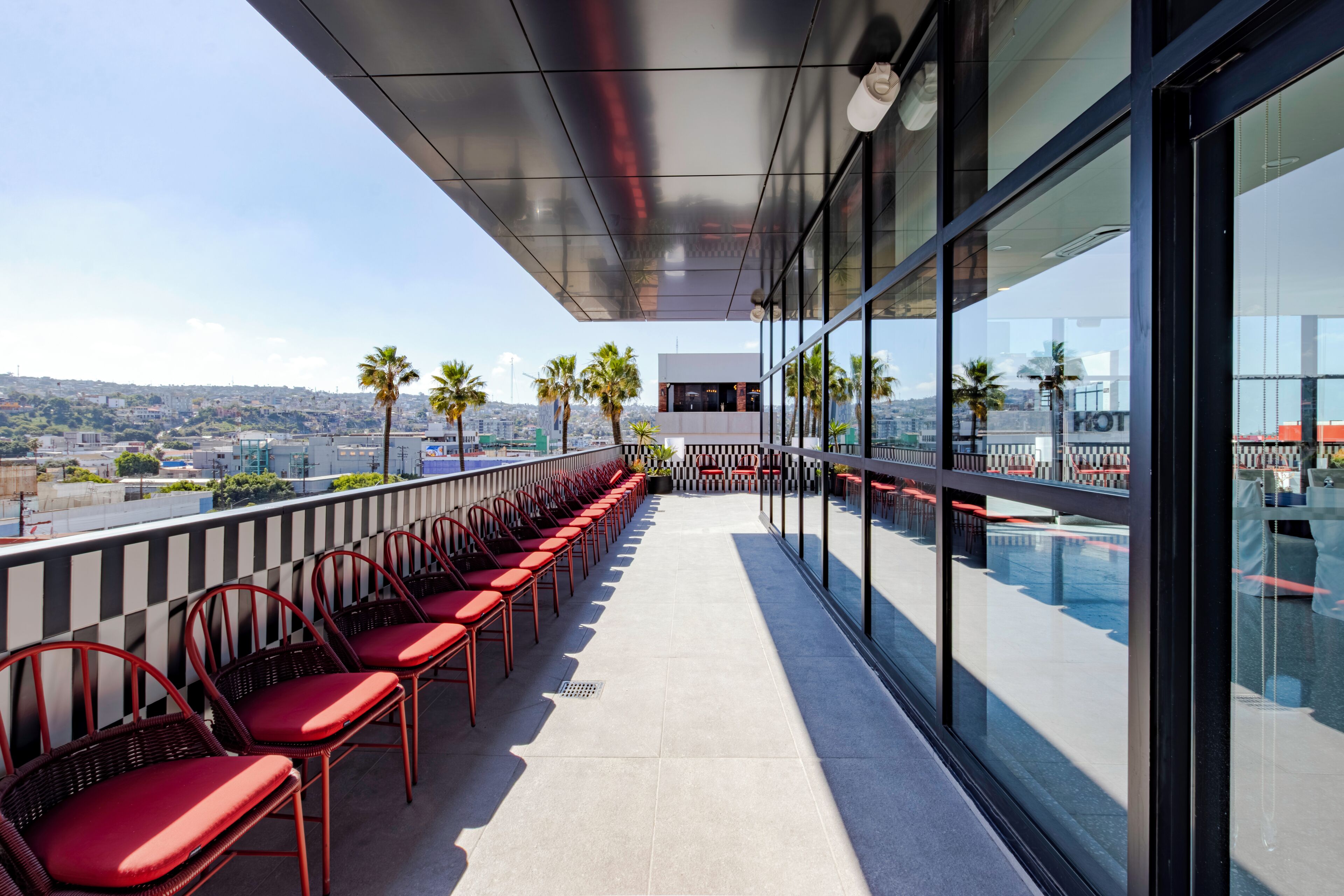 A rooftop terrace with red chairs, a pool, and a city view.