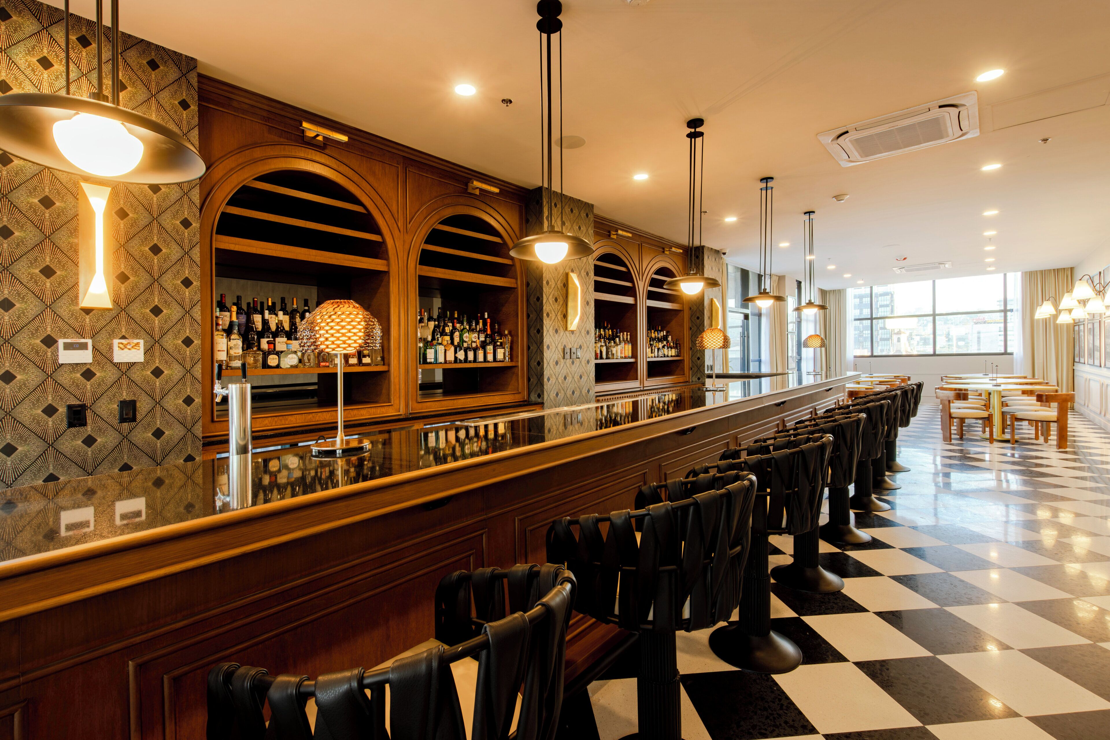 Uma área de bar com piso quadriculado, balcão de madeira e diversos arranjos de assentos.
