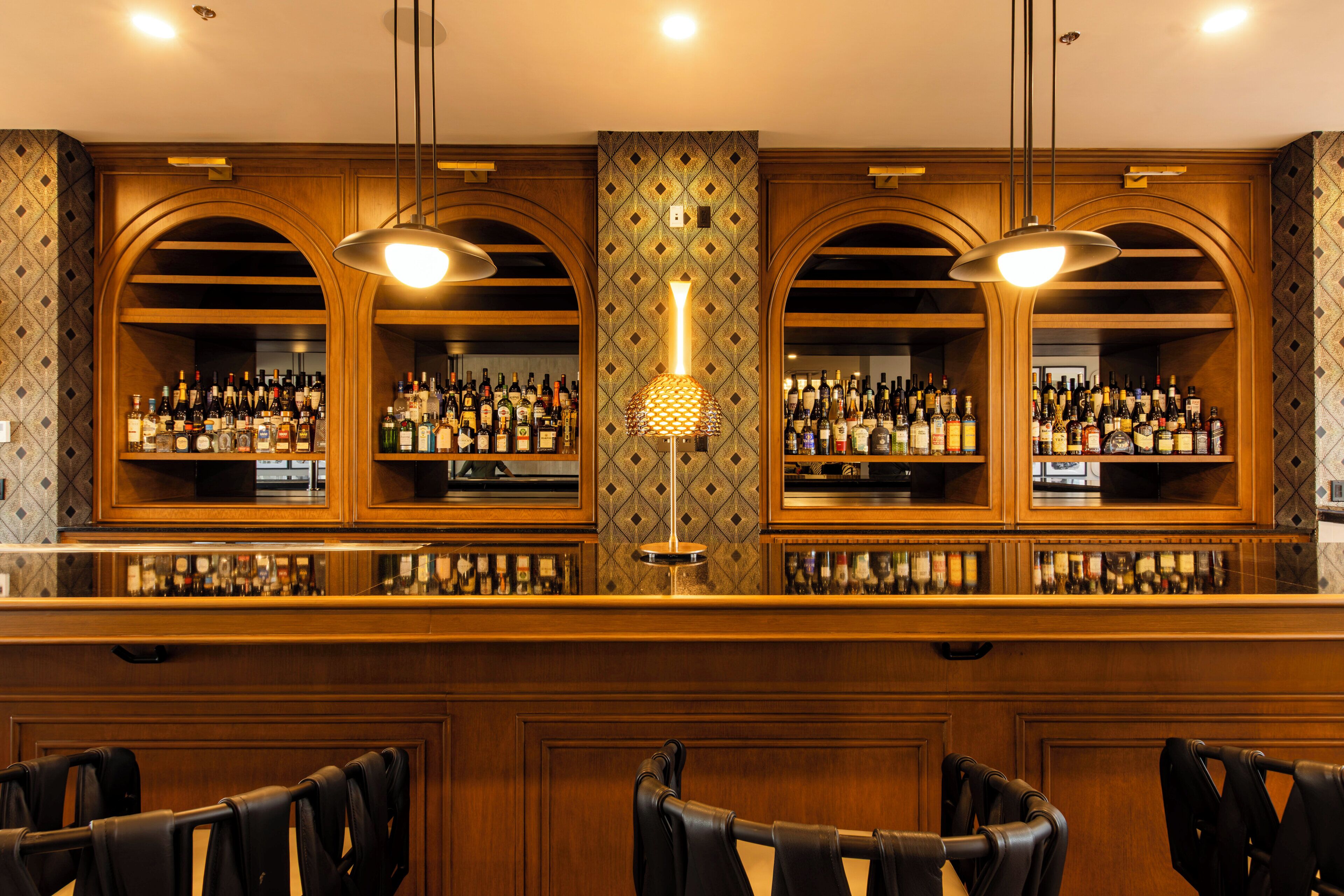 A bar area with wooden cabinets, shelves of bottles, and two pendant lights.