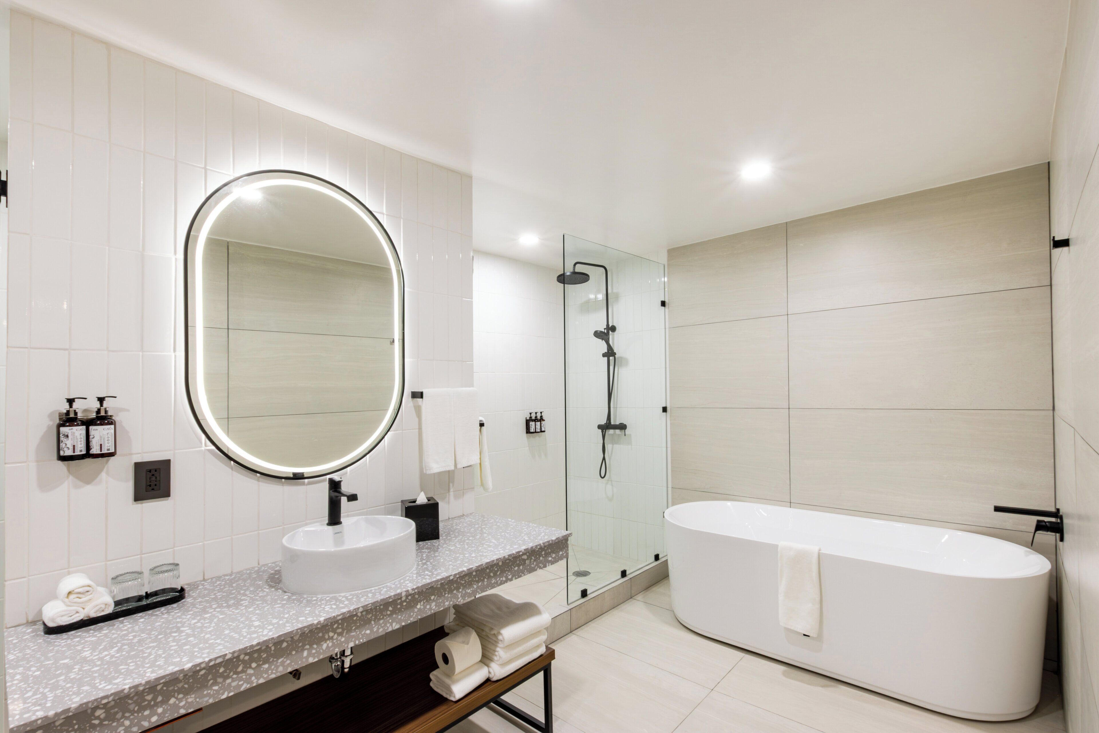 Un baño moderno con una bañera independiente, un espejo redondo y una zona de ducha con mampara de vidrio.