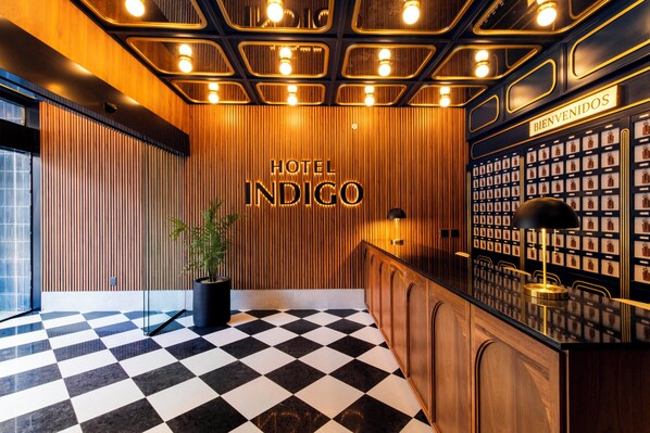 Un vestíbulo de hotel con suelo a cuadros, paneles de madera, un mostrador de recepción y una pared decorada con llaveros.