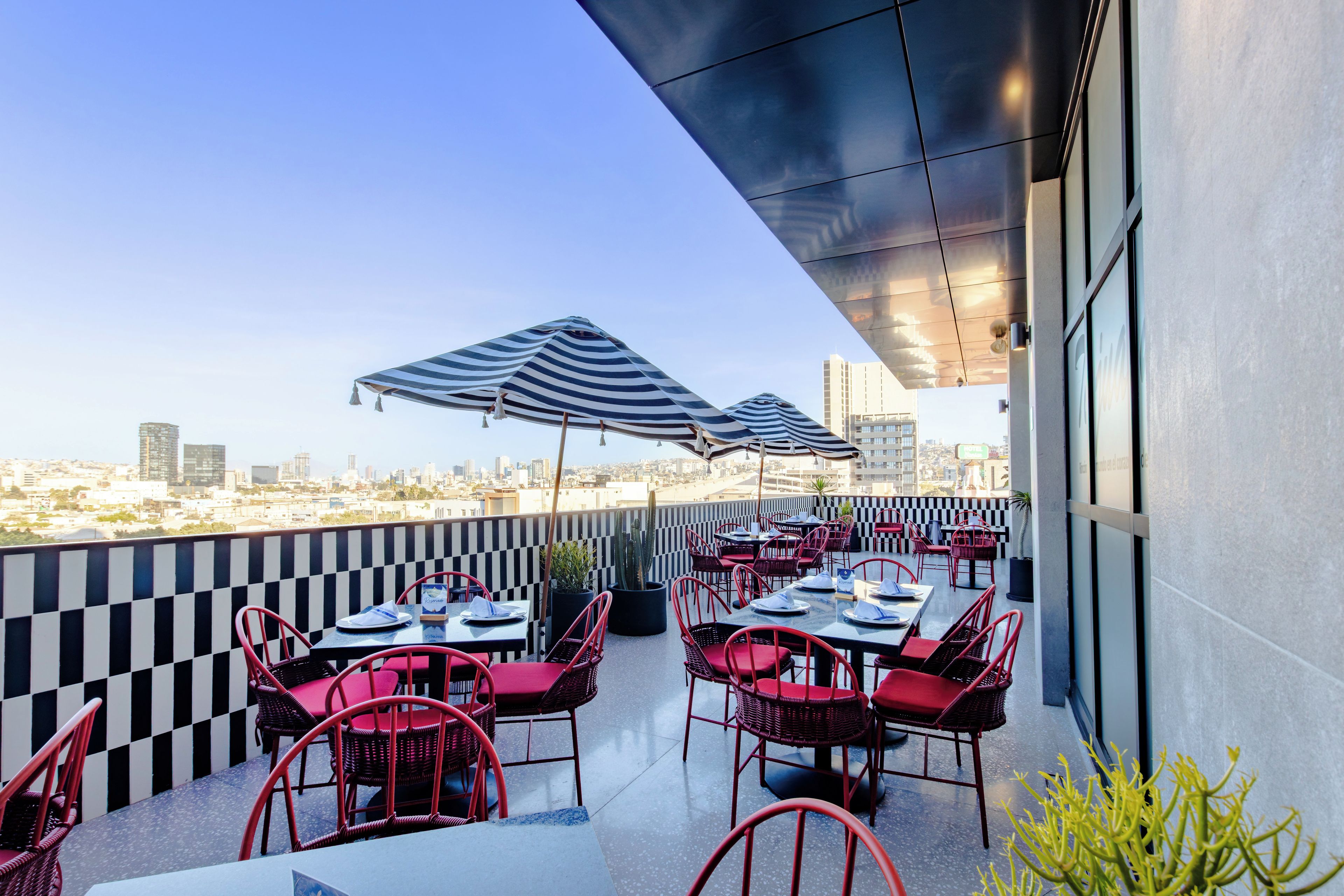 Un espace extérieur aménagé pour les repas, avec des tables, des chaises, des parasols et une vue sur la ville.