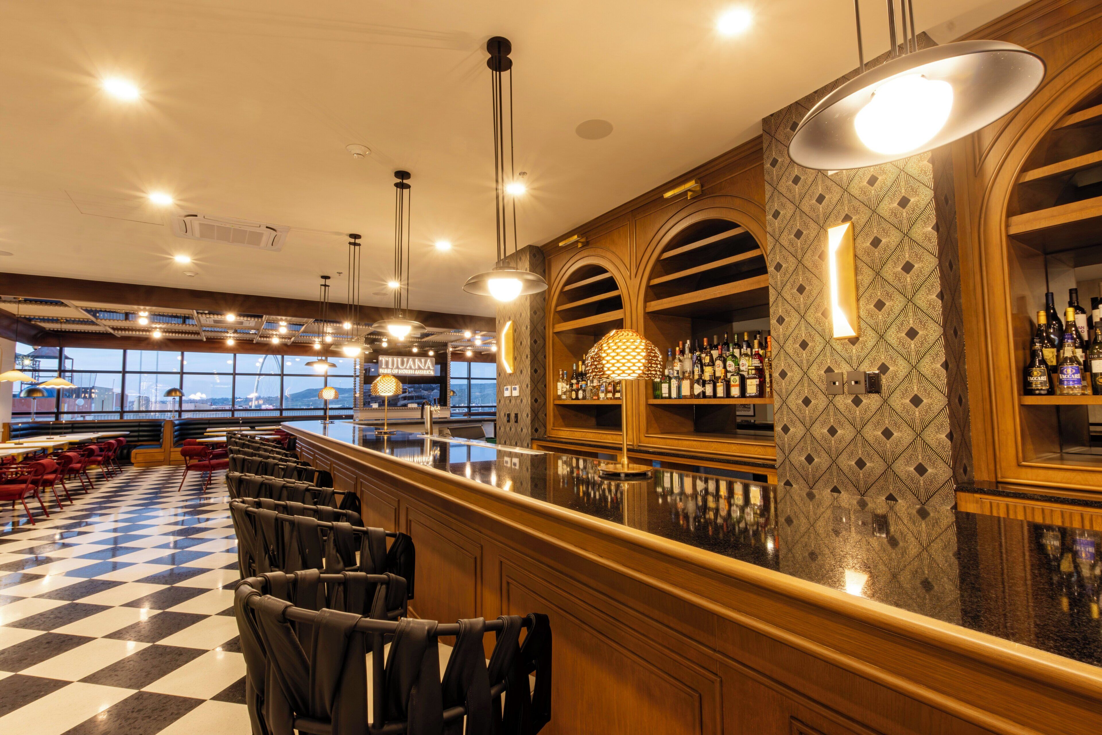 A bar area with a checkered floor, bar stools, and a bar counter with bottles.
