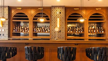 Una zona de bar con paneles de madera, varias estanterías llenas de botellas y taburetes acolchados negros.