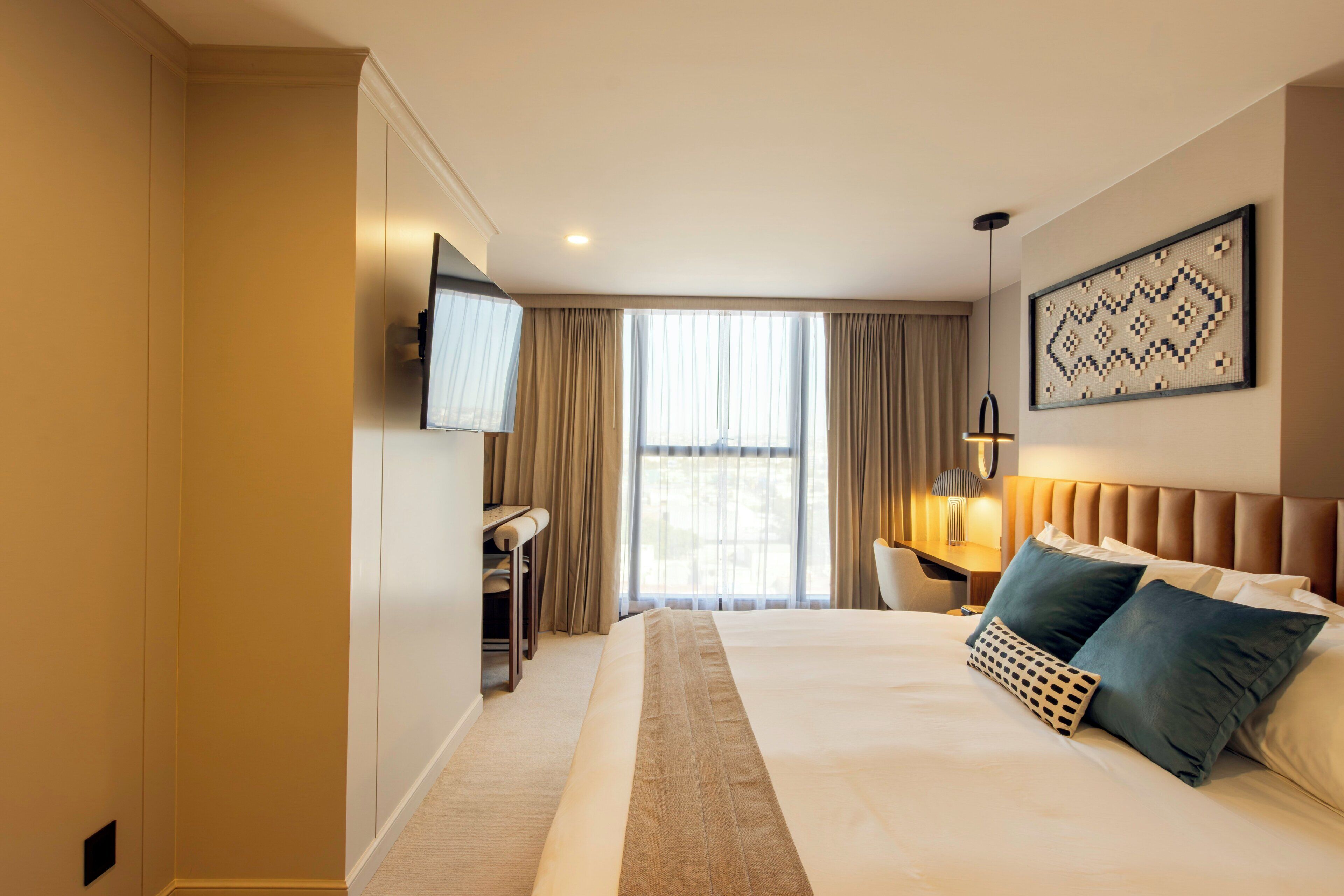 Habitación de hotel con una cama grande, un escritorio, una silla, un televisor y una ventana con cortinas.