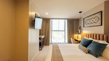 Habitación de hotel con una cama grande, un escritorio, una silla, un televisor y una ventana con cortinas.