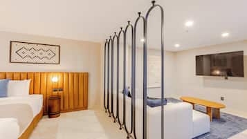 Habitación de hotel moderna con cama, sofá, banco, televisor y un elemento decorativo en la pared.