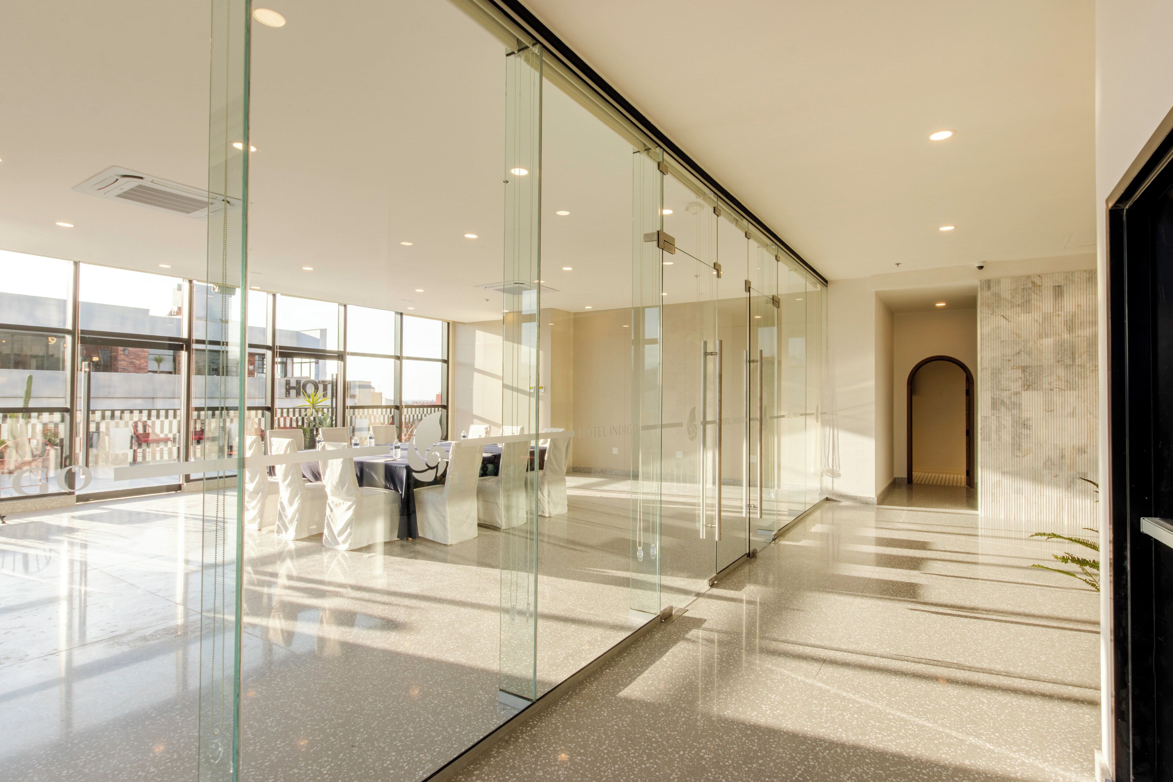 Un hall d’hôtel moderne avec des murs en verre, un comptoir d’accueil et un espace détente avec des fauteuils.