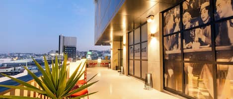 Exterior de un hotel con balcón, vista a la ciudad y una pared con fotografías.