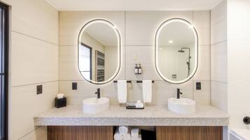 A modern bathroom with two sinks, a large mirror, and a shower.