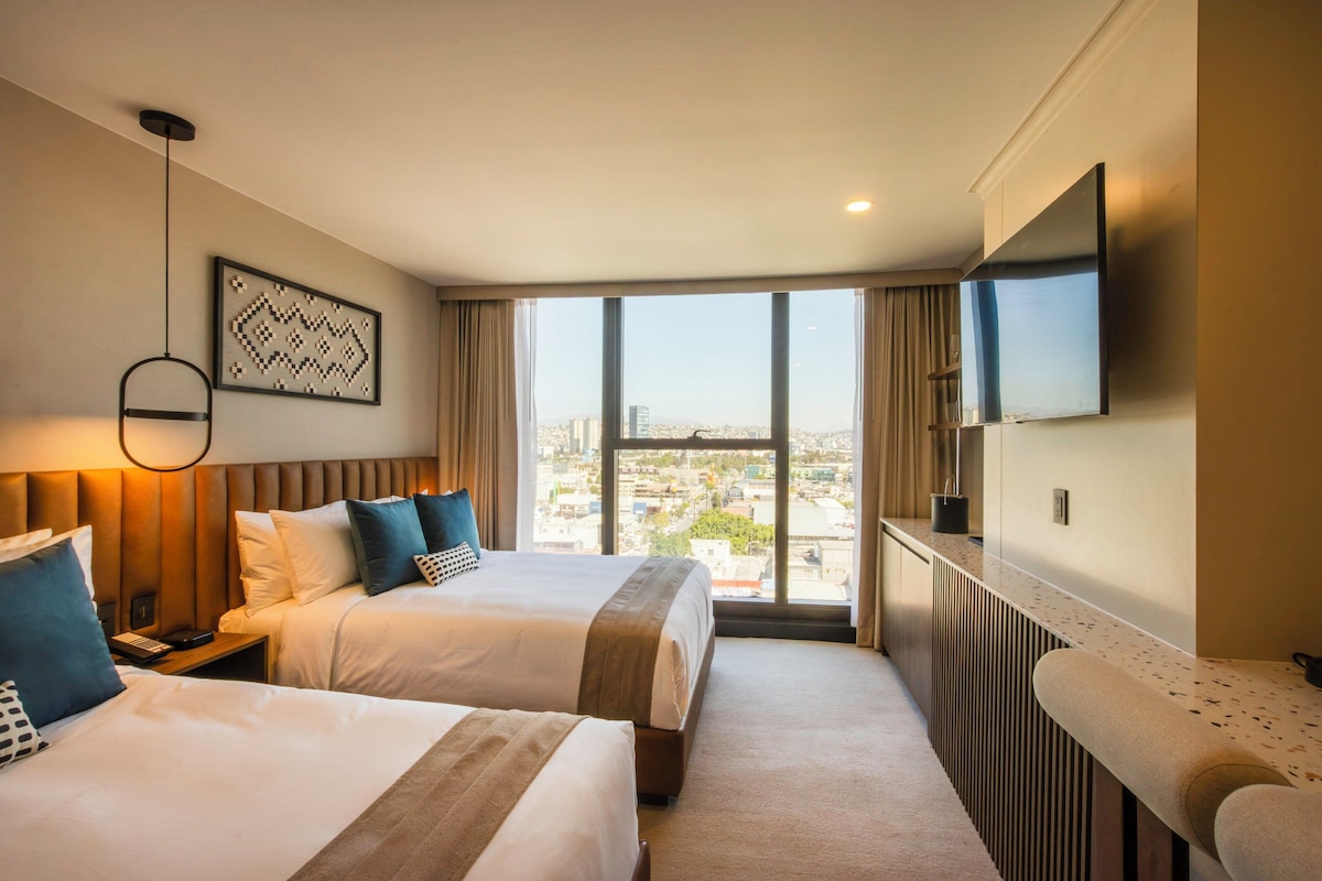 Habitación de hotel con dos camas, televisión y vista a la ciudad.