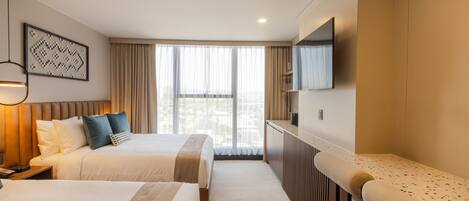 Une chambre d’hôtel avec deux lits, une télévision, un bureau et une fenêtre avec des rideaux.