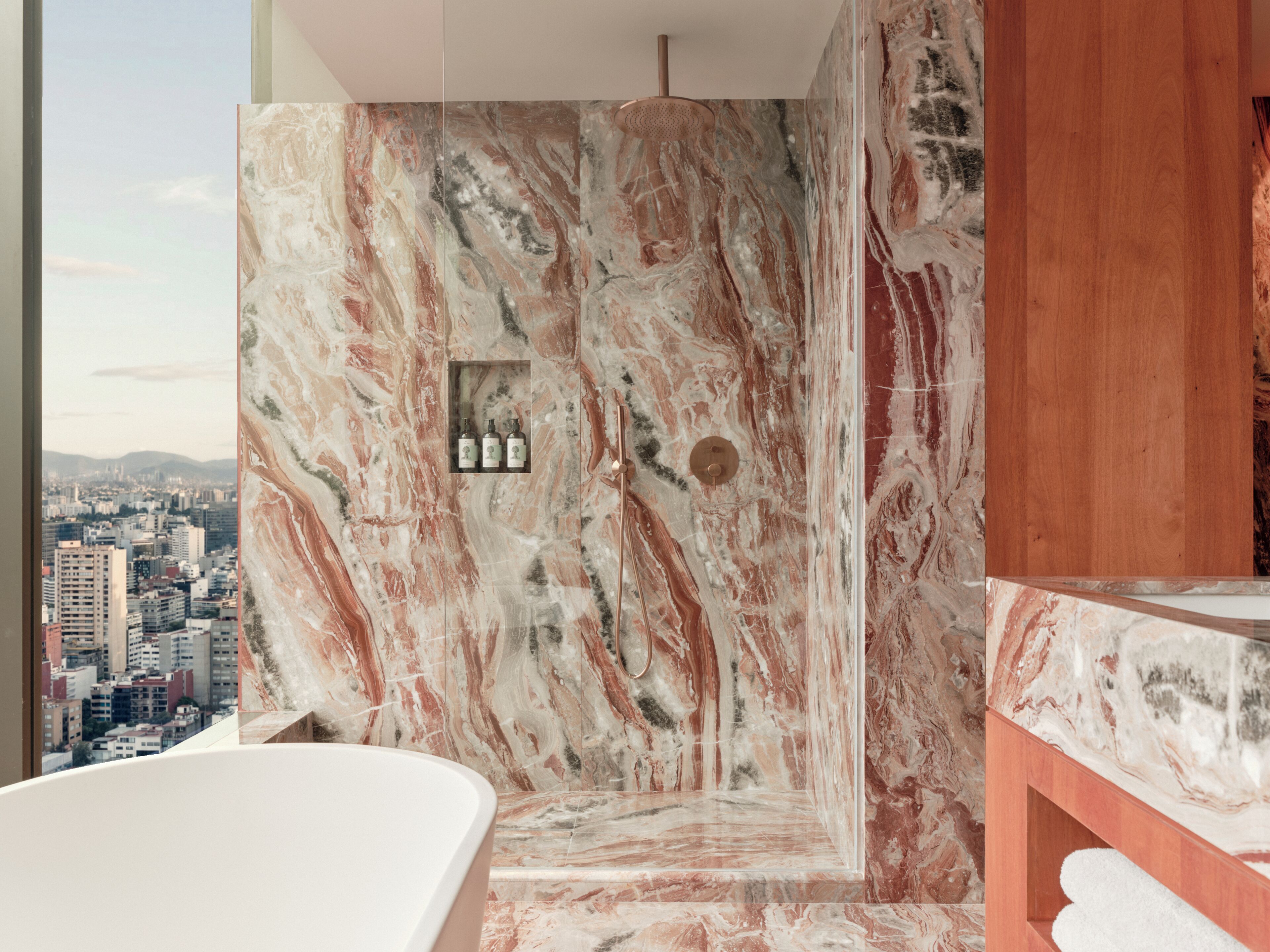Un baño con pared de mármol, ducha y vistas a la ciudad.