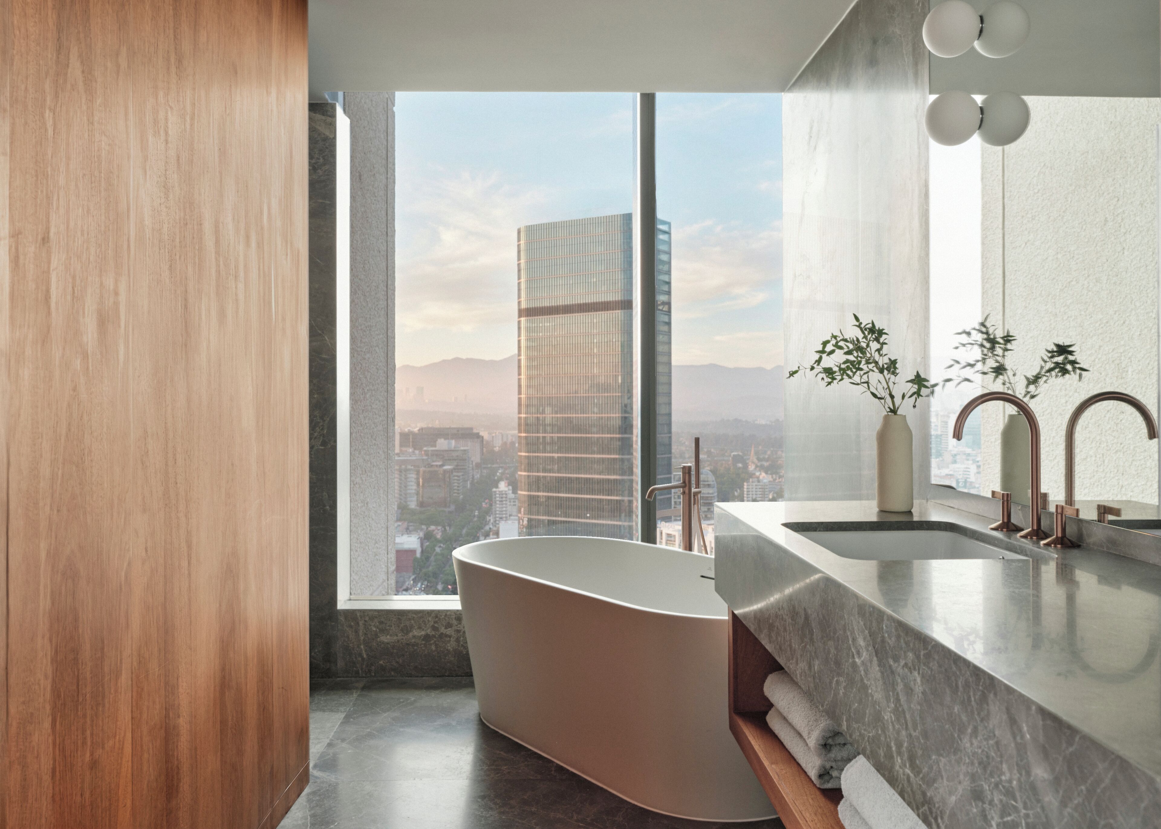 A modern bathroom with a freestanding bathtub, a large mirror, and a view of a cityscape through a large window.