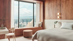 Ein modernes Hotelzimmer mit großem Fenster, einem Bett, einem Schreibtisch und einem Sessel.