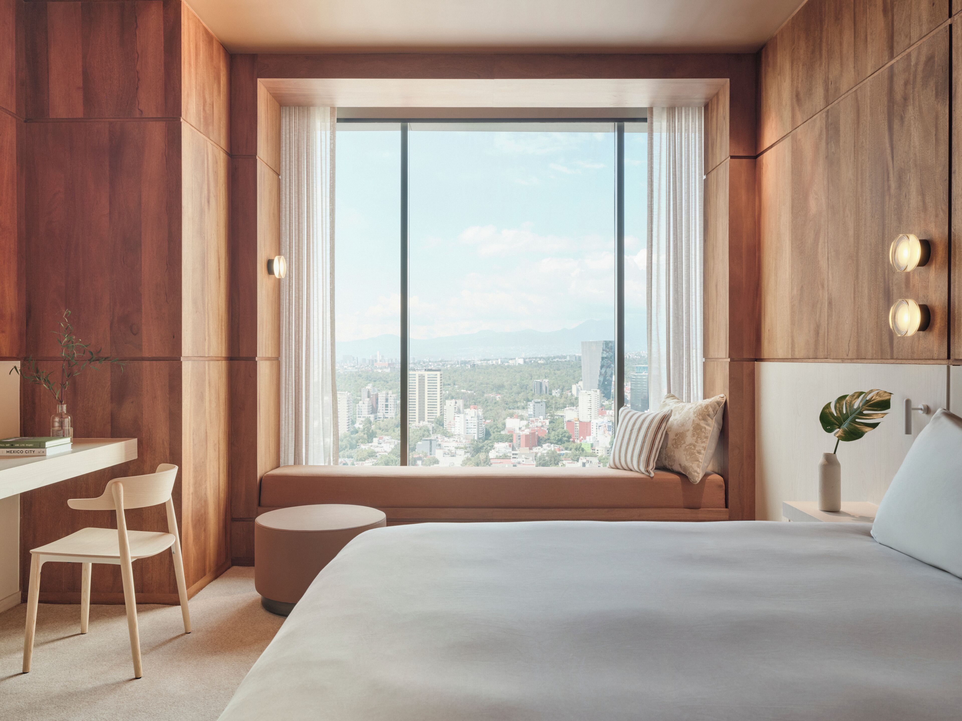 Una habitación de hotel moderna con un gran ventanal, una cama, un escritorio y una silla.