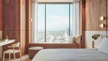 Una habitación de hotel moderna con un gran ventanal, una cama, un escritorio y una silla.