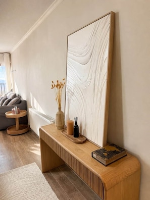 Una sala de estar moderna con un banco de madera, un cuadro abstracto grande y un jarrón con flores secas.