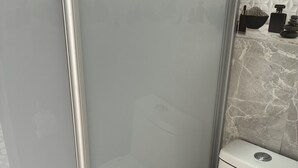 Kylpyhuone, jossa on wc, lasinen suihkuseinä ja marmorikuvioitu seinä.