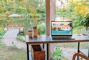 Ein Laptop auf einem Tisch, der eine Webseite über Deltsville, Virginia, anzeigt, mit Blick auf einen Garten und eine Anlegestelle mit Stühlen.