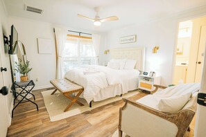 Ein Schlafzimmer mit Bett, einer Bank, einem Nachttisch, einem Deckenventilator und Blick ins Freie.
