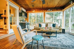 Ein gemütliches Wohnzimmer mit Holzbalkendecke, einer Sofagarnitur, einem Couchtisch und einem großen Fenster mit Blick ins Freie.