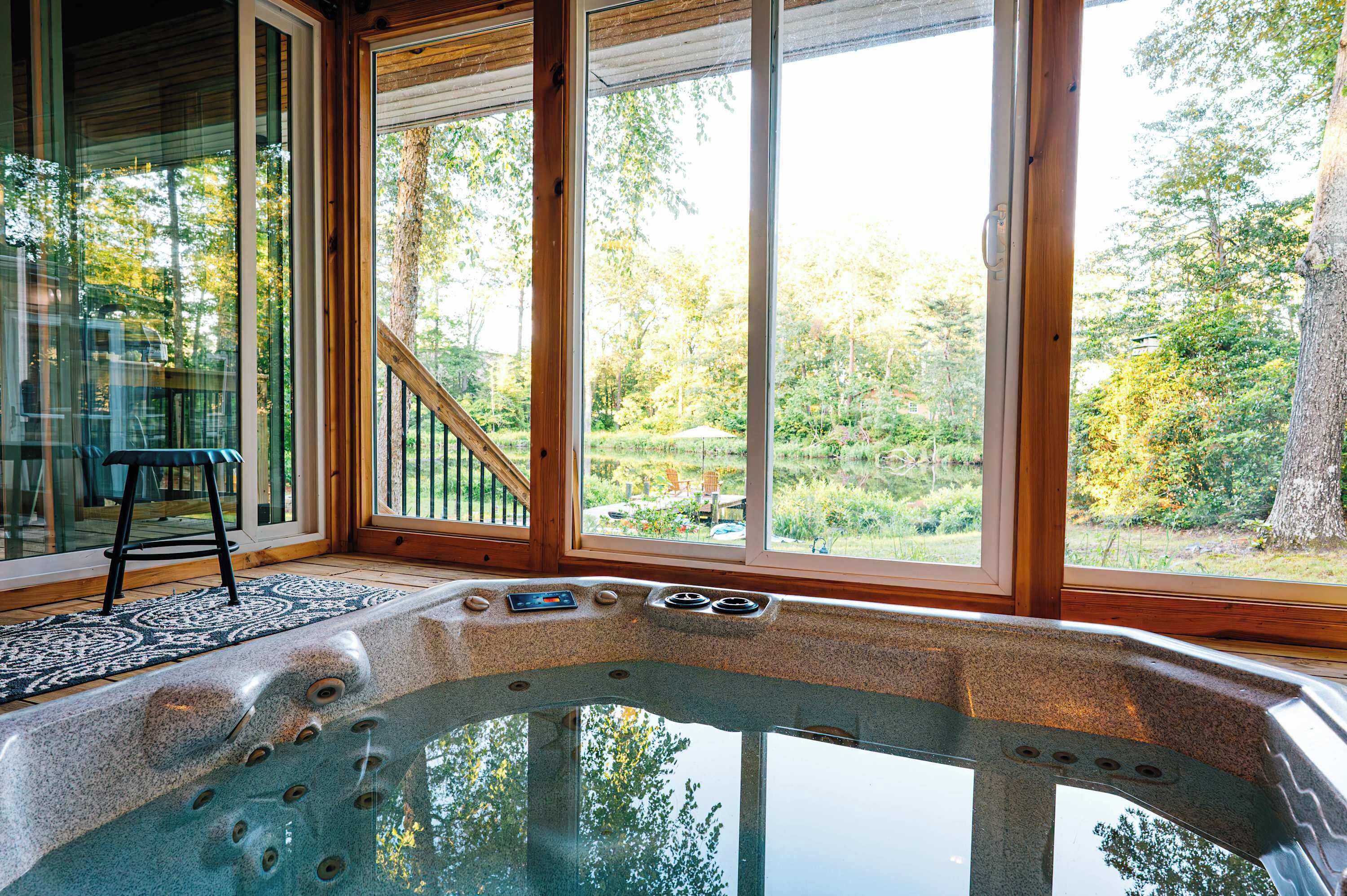 Un jacuzzi con vistas a una zona boscosa a través de amplios ventanales.