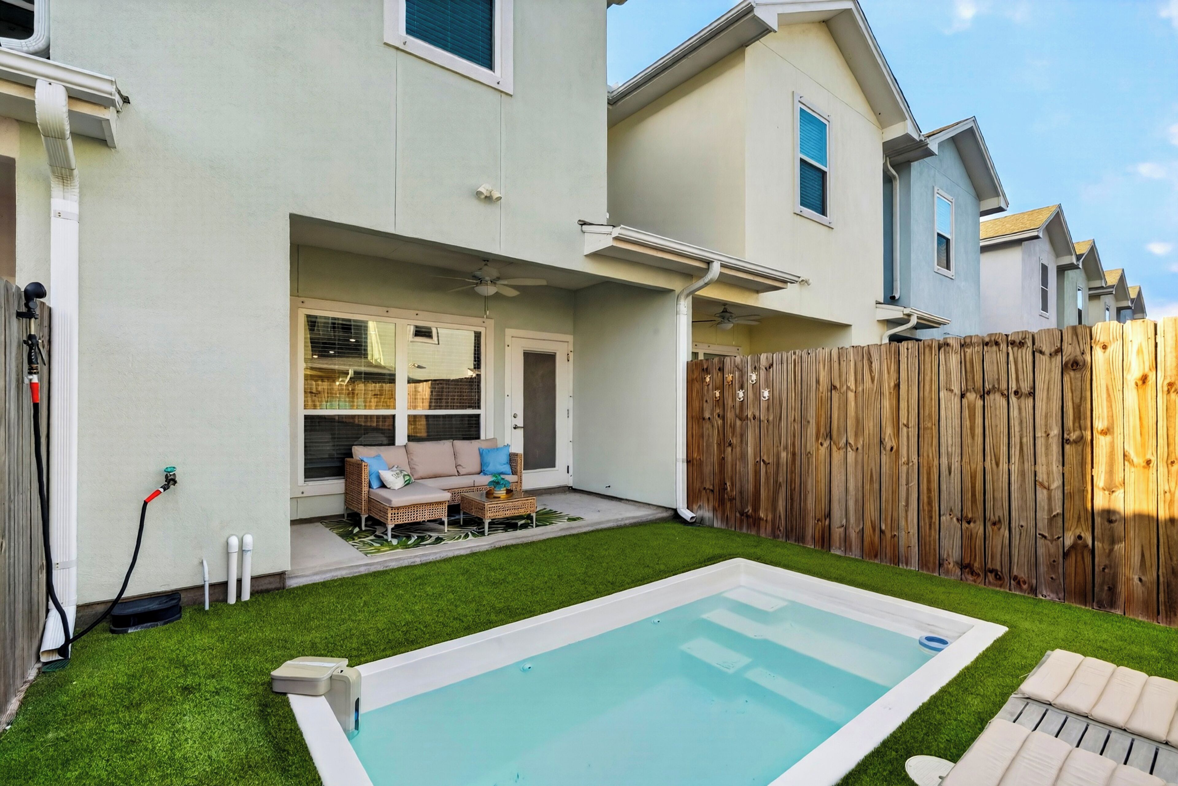 A residential backyard with a swimming pool, a wooden fence, and a patio area with outdoor furniture.