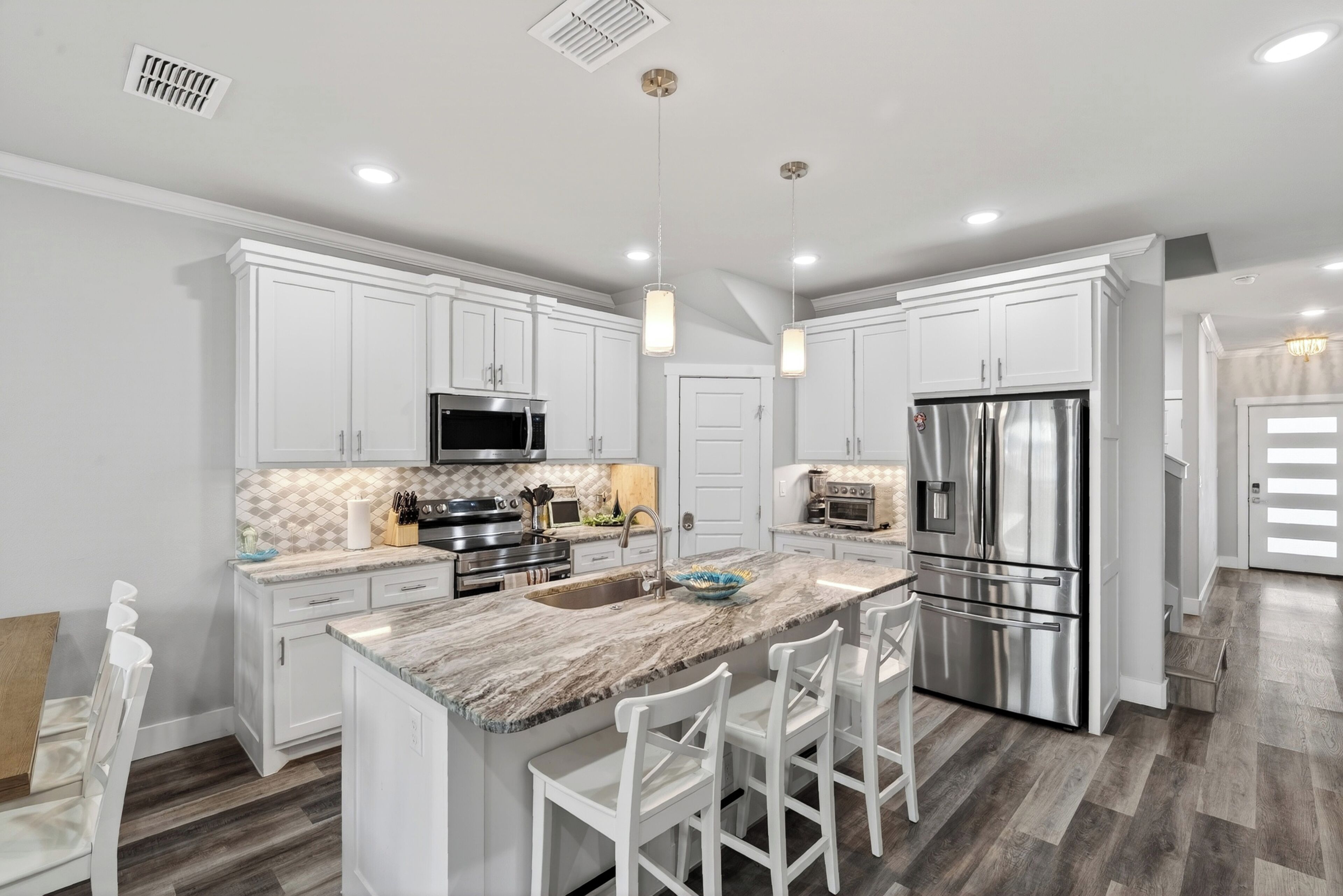 A modern kitchen with white cabinetry, stainless steel appliances, a marble island, and pendant lighting.