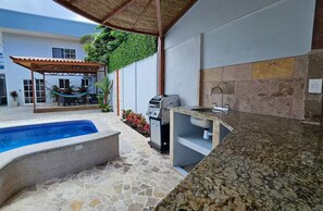 Ein Pool mit Steinbord, ein Grill und eine Spüle mit Steinrückwand.