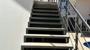 Een reeks buitentrappen die leiden naar een gebouw, met een metalen leuning en een heldere lucht op de achtergrond.
