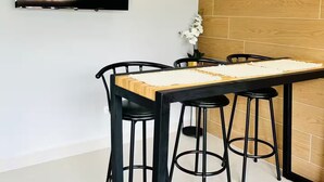 Ein moderner Essbereich mit Holztisch, schwarzen Stühlen, einem an der Wand montierten Flachbildfernseher und einer Wand aus Ziegelsteinen.