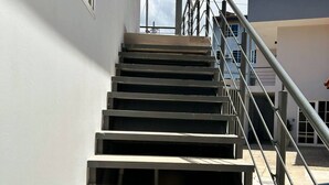 Eine Treppe aus Beton führt zu einem Hauseingang, mit einem Metallgeländer auf der rechten Seite und einer weißen Wand auf der linken Seite.