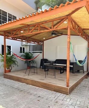 Eine Terrasse im Freien mit einer Holz-Pergola, zwei Hängematten, einem schwarzen Sofa und einem Grill.