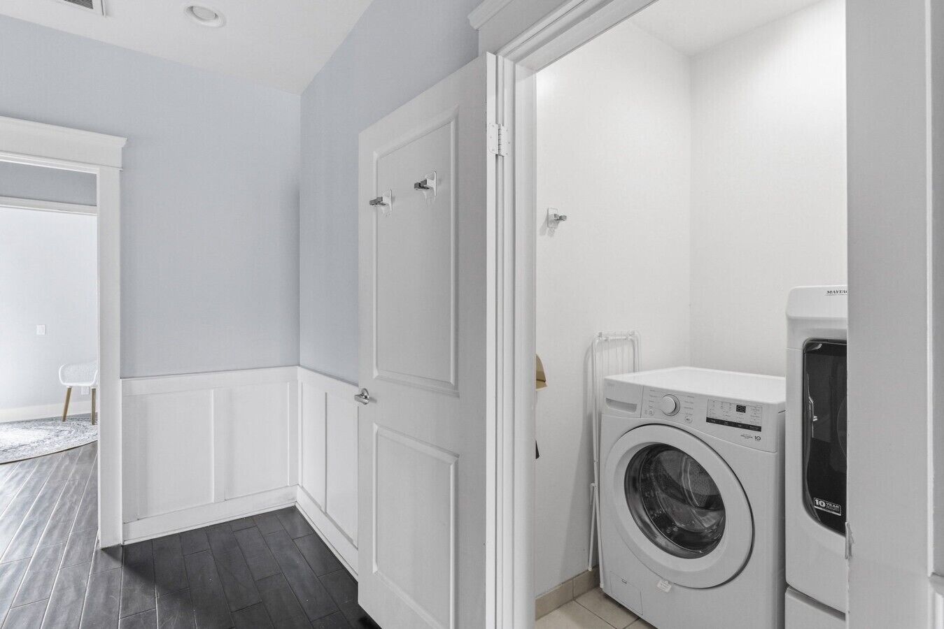 Une buanderie équipée d’un lave-linge à chargement frontal, d’un sèche-linge et d’une porte donnant sur une autre pièce.