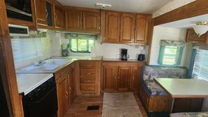 Cozinha compacta de RV com armários de madeira, pia, fogão e um pequeno espaço de estar com mesa.