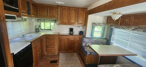 A compact RV kitchen with wooden cabinets, a sink, a stove, and a small seating area with a table.