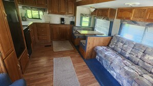 Uma cozinha compacta para motorhome, com armários de madeira, fogão embutido e área de refeições.