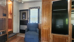 Um quarto compacto com um armário de madeira, uma cadeira azul e uma televisão preta.