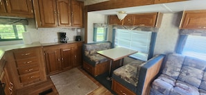 Cocina compacta para autocaravana con armarios de madera, una cafetera y una pequeña mesa.