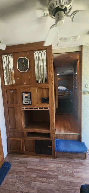 Habitación con una unidad de pared de madera, un reloj, un ventilador de techo y una zona alfombrada azul.