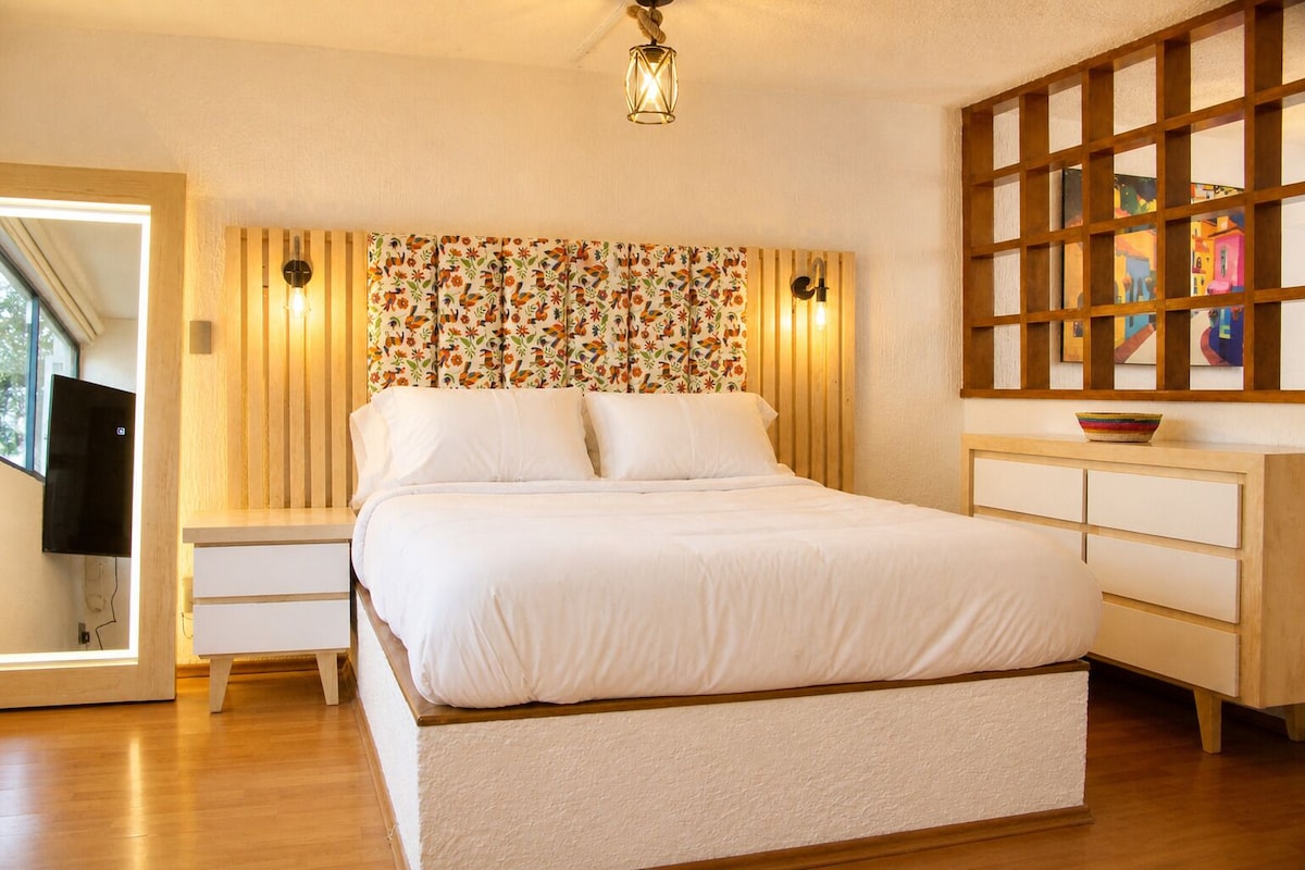 Een slaapkamer met een bed, nachtkastjes, een dressoir, een tv aan de muur en een raam.