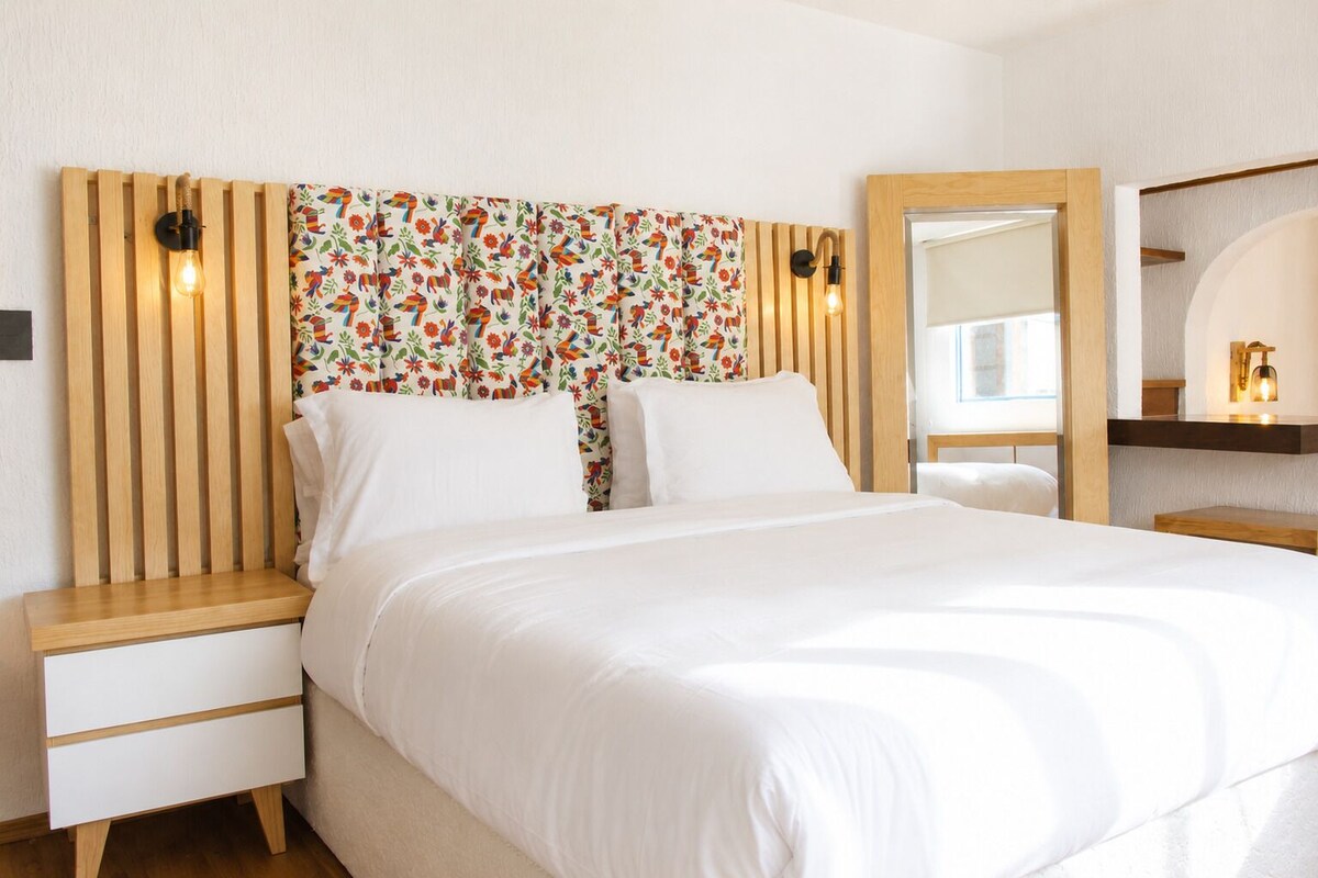 Een bed met witte beddengoed, een houten hoofdbord met verticale latten en een gordijn met bloemenprint.