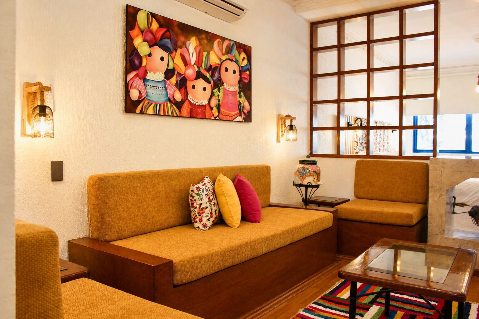 A living room with a sofa, armchairs, a glass coffee table, a colorful rug, and a large painting on the wall.