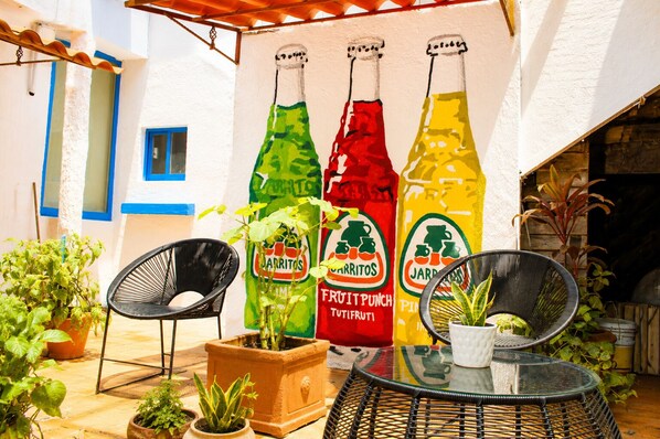 A patio with three large bottles of beverages, two chairs, and potted plants. - El Rincon Mexicano Polanco by RUZ (Ciudad de México)