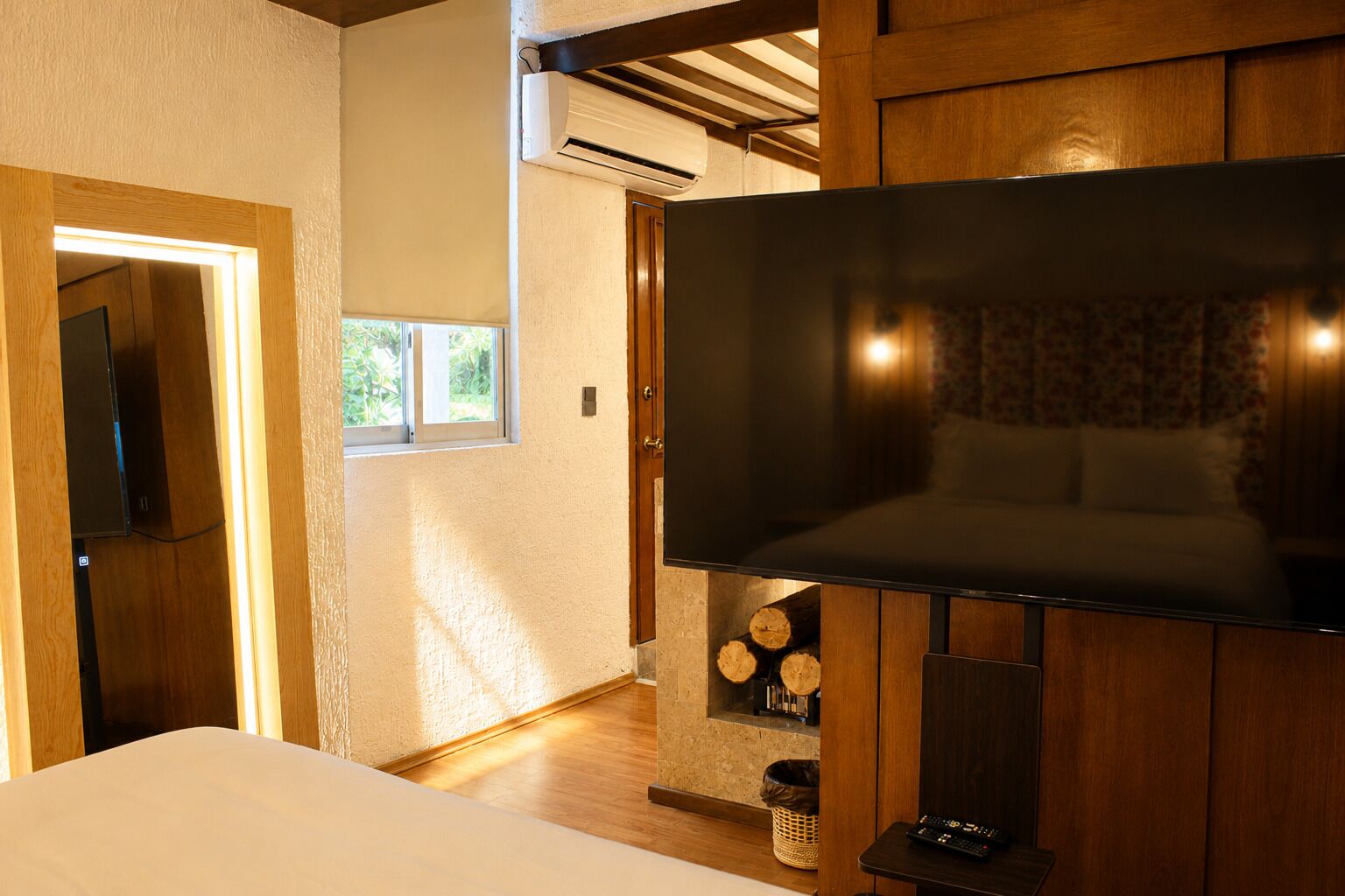 A room with a large flat-screen TV mounted on a wooden wall, a door leading to another room, and a window allowing natural light.