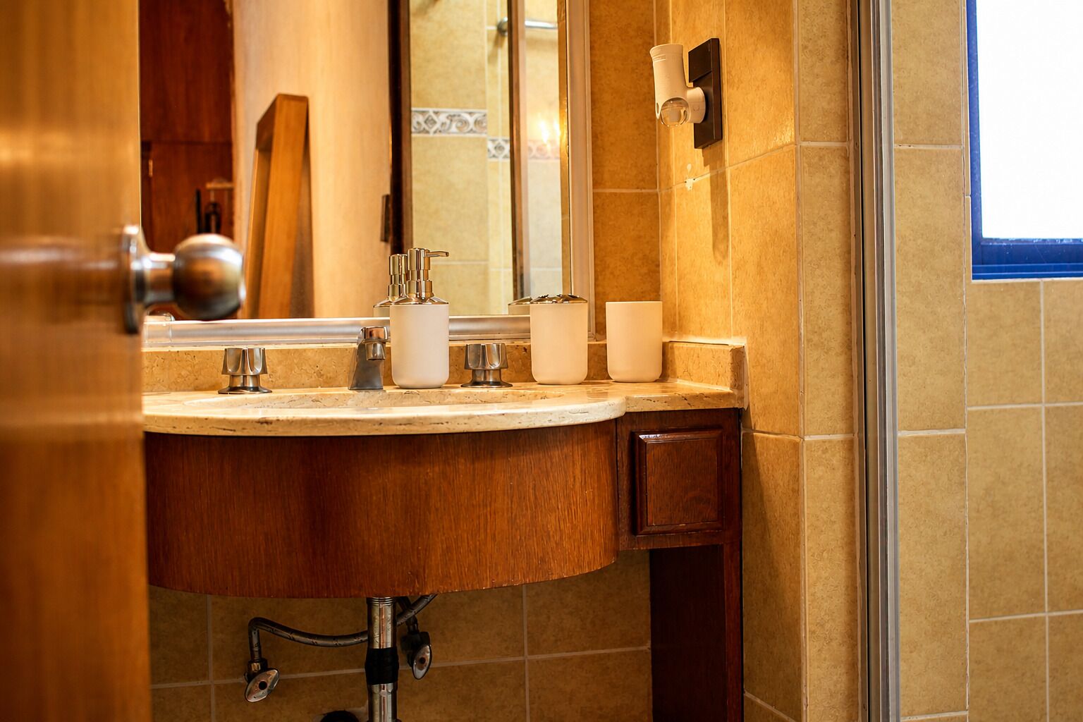 A bathroom with a wooden vanity, a mirror, and a wall-mounted light fixture.