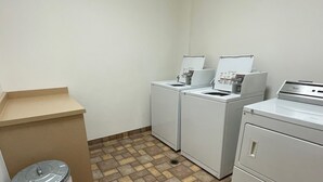A laundry room with two washing machines, a dryer, and a trash can. - Historic Warehouse converted into Cozy Boutique Loft 305 (Fargo)