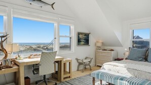 Un dormitorio con escritorio, silla, cama y vista al océano.